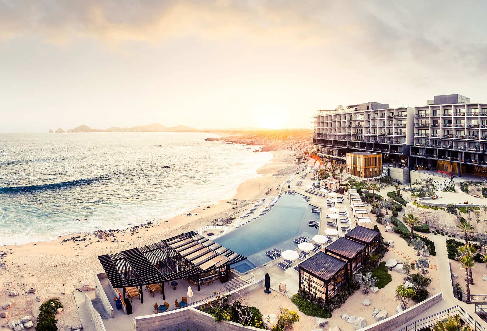 Modern Luxury Meets Cabo Vibes at The Cape: Guests relaxing by the stunning infinity pool with the Cabo San Lucas skyline in the background